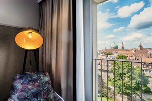 Quarto com vista para a cidade, luminária, cadeira e janela com cortinas.