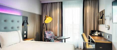A hotel room with a bed, a desk, a chair, a desk lamp, a television, and a window with curtains.