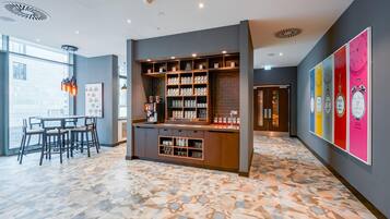 Uma área de bar moderna com prateleiras cheias de canecas e copos, um espaço de estar com mesas e cadeiras, e uma parede colorida com relógios.