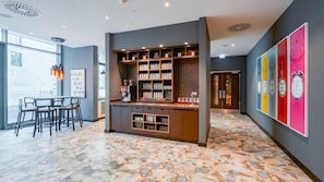 A modern bar area with shelves of mugs and glasses, a seating area with tables and chairs, and a colorful wall with clocks. - Premier Inn Nürnberg City Opernhaus (Nuremberg)
