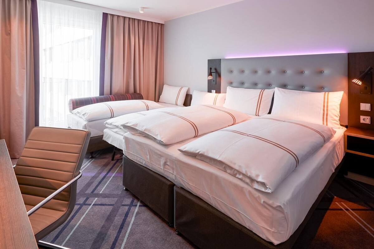 A hotel room with two beds, a chair, a desk, and a wardrobe.