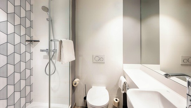 Un baño moderno con ducha, inodoro y lavabo, que presenta un diseño de baldosas geométricas en las paredes.