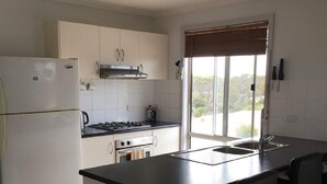 Eine moderne Küche mit einer zentralen Kochinsel, Barhocker, Kühlschrank, Herd, Backofen und einem Fenster mit Blick.