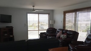 Ein Wohnzimmer mit einem dunkelgrauen Sofa, einem Holzesstisch und einem an der Wand befestigten Fernseher.