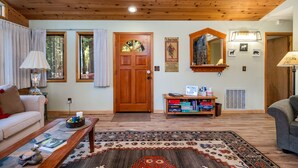 Ein gemütliches Wohnzimmer mit Holzbalkendecke, Kamin aus Stein, einer Holztür und einem Bücherregal mit Gesellschaftsspielen.