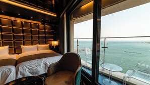 A modern hotel room with a large bed, a seating area with a chair and a table, and a balcony with a view of the sea. - Best Louis Hamilton Hotel Ocean Terrace (Busan)
