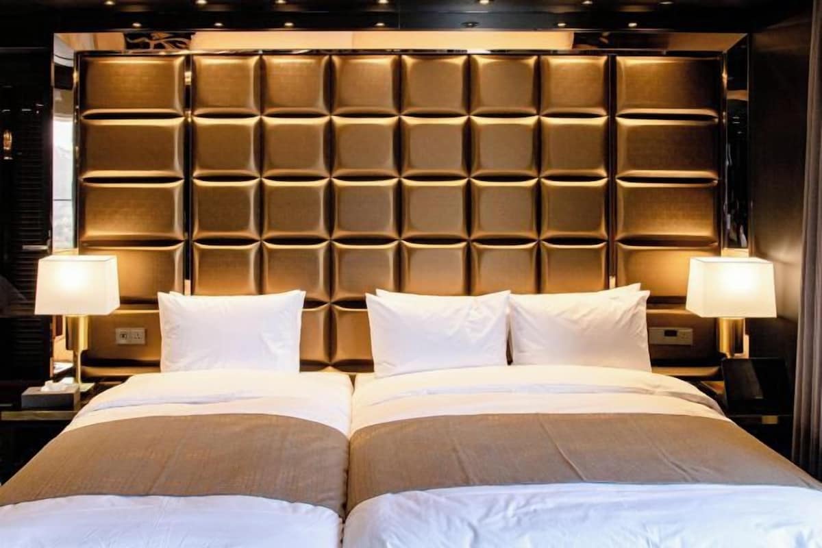 Une chambre d’hôtel avec un grand lit, deux tables de chevet et une tête de lit ornée d’un motif quadrillé.