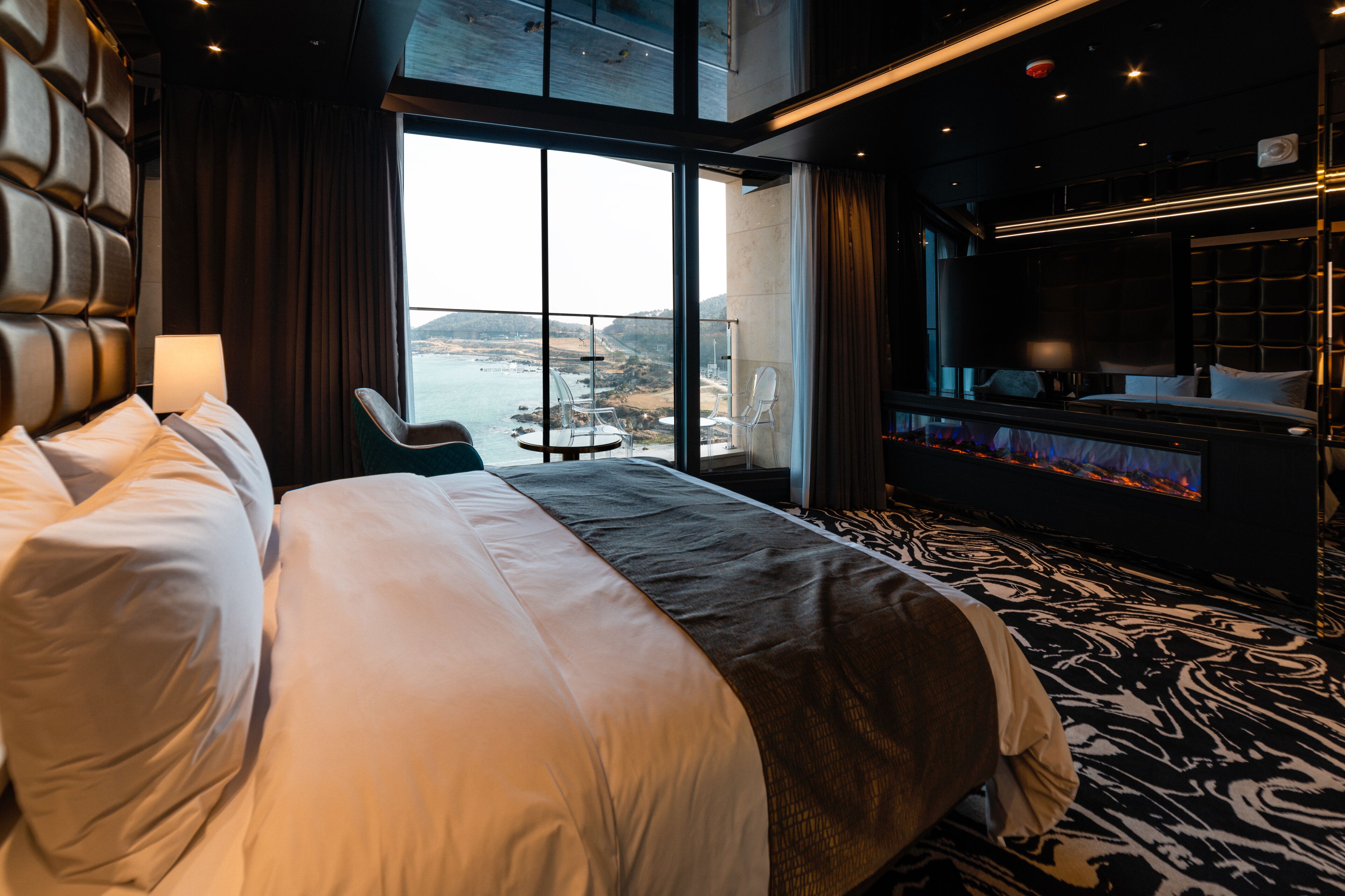 A modern hotel room with a large bed, a TV, and a view of the sea.