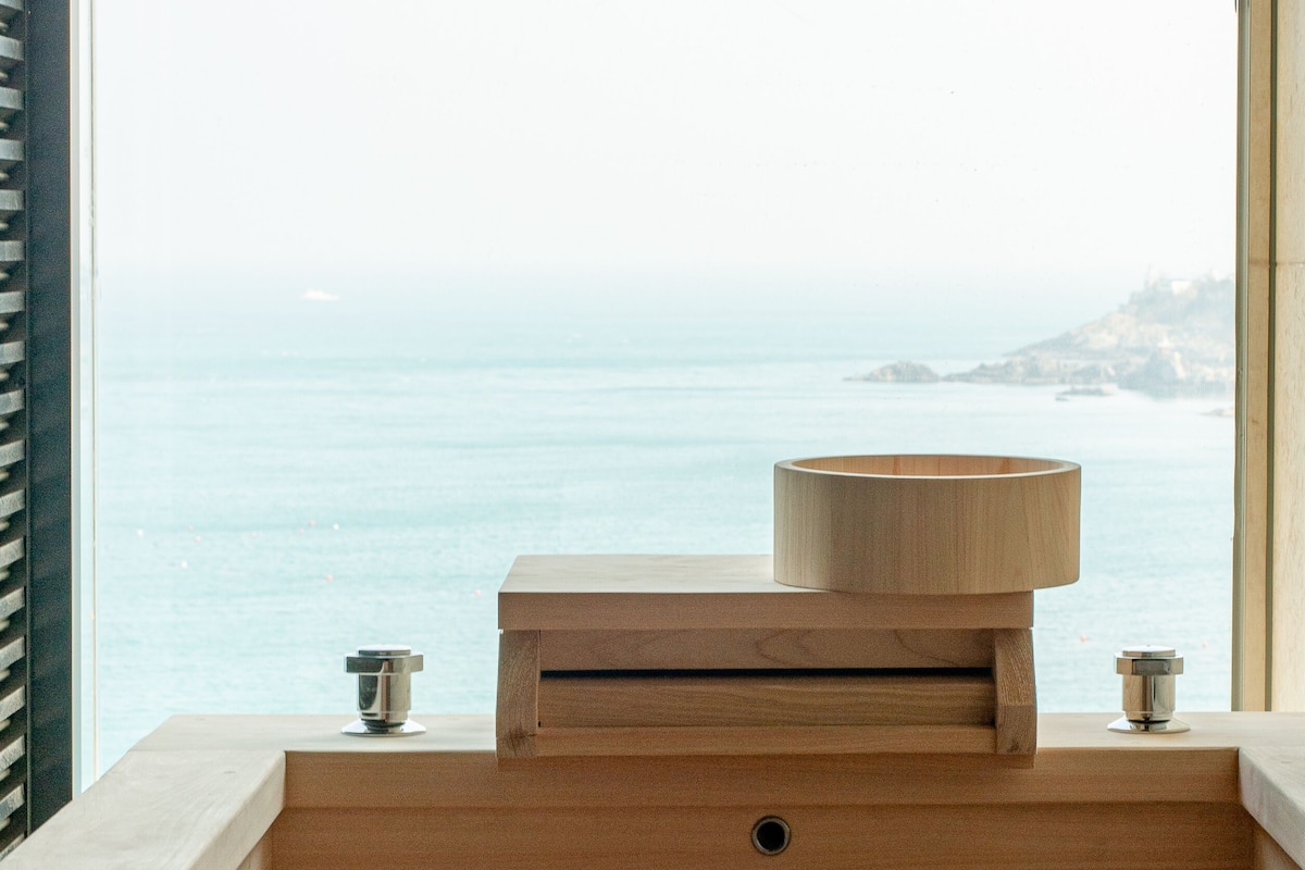 A wooden vanity with a sink and a wooden bowl on top, overlooking a body of water.