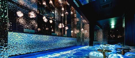 A modern interior with a reflective wall, hanging spherical lights, and a patterned floor.