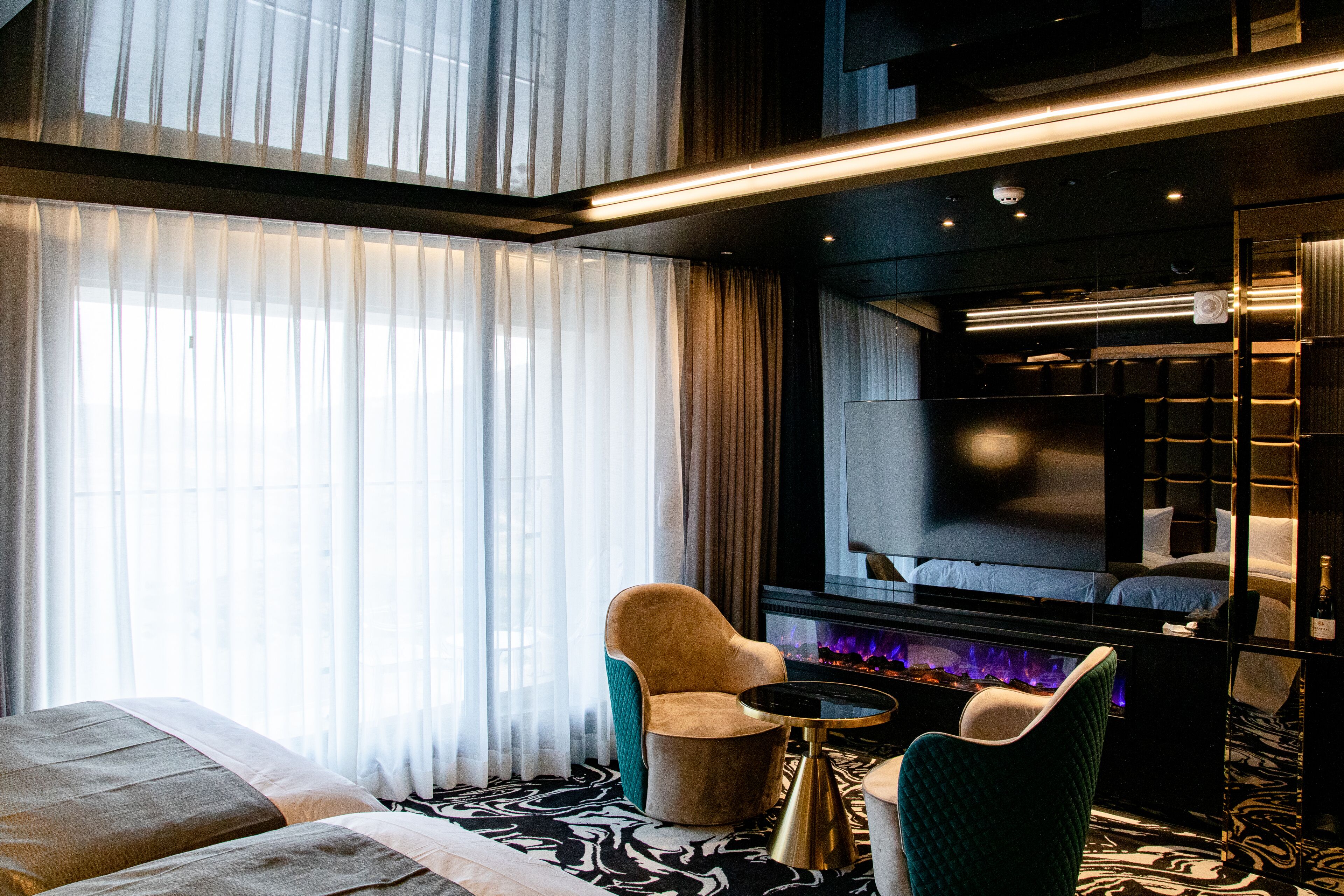 A modern hotel room with a large bed, a seating area with a small table, and a fireplace.