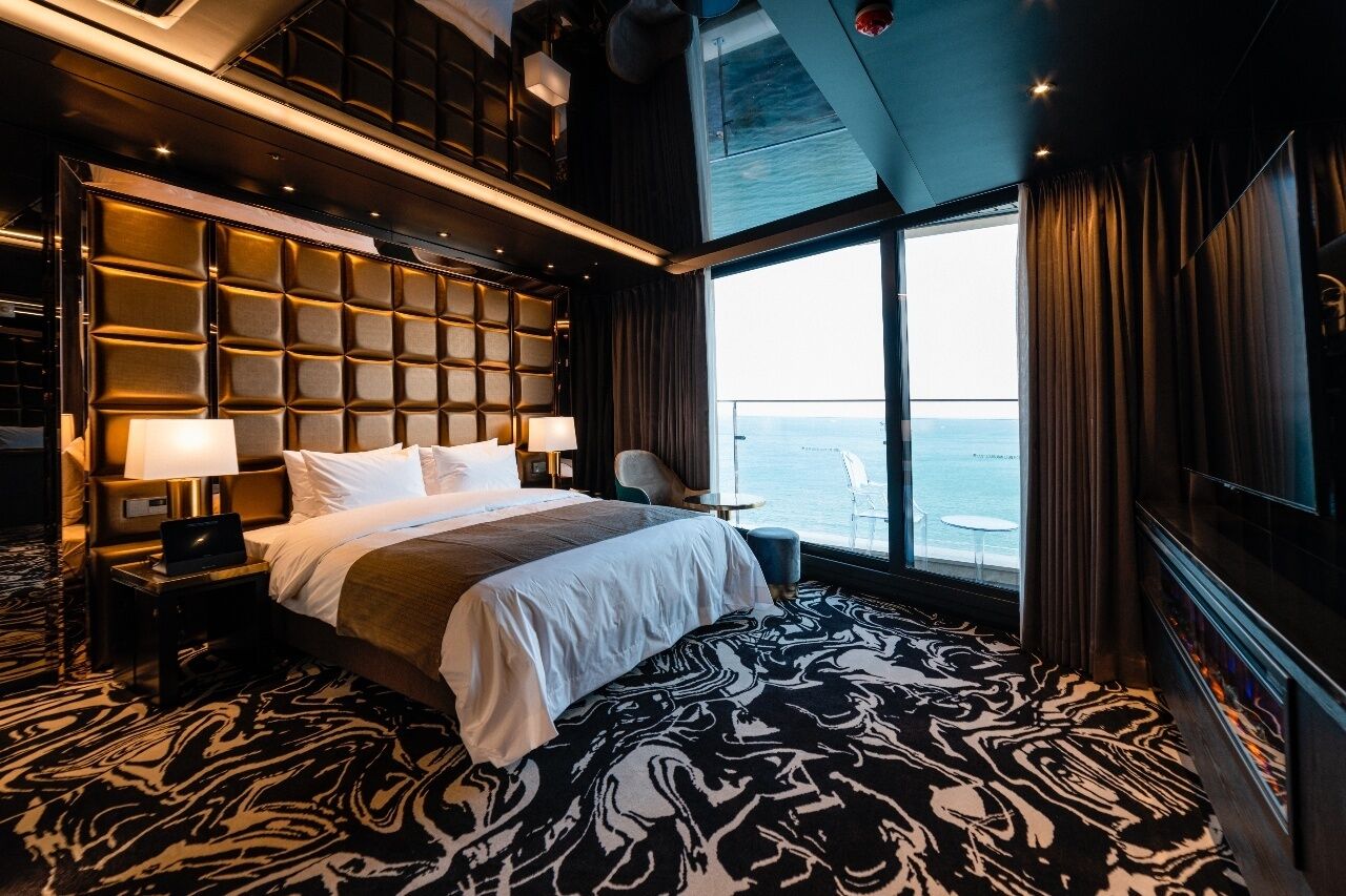Een luxueuze hotelkamer met een groot bed, uitzicht op zee, een zithoek met een tafel en een modern design.
