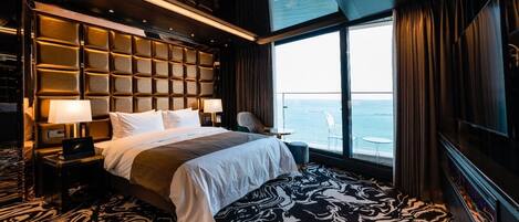 Een luxueuze hotelkamer met een groot bed, uitzicht op zee, een zithoek met een tafel en een modern design.