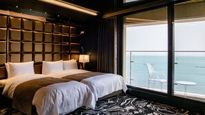 A hotel room with a large bed, a view of the sea, and a balcony with a chair and table. - Best Louis Hamilton Hotel Ocean Terrace (Busan)