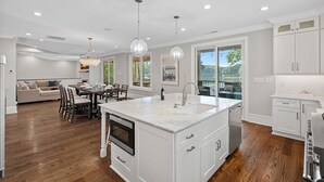 Moderni keittiö, jossa on valkoiset kaapit, suuri keittiösaareke, jossa on pesuallas, ja riippuvalaisimet.