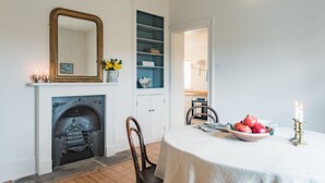 A dining room with a fireplace, a mirror, a bookshelf, and a table set for a meal. - West Cottage -  charming seaside cottage by Bloom Stays - 4 guests  in 2 bedrooms (Dungeness)