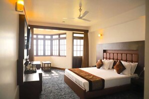A hotel room with a large bed, a desk with toiletries, a ceiling fan, and a view of the outside through large windows. - Jewel Himalayan Heights (Gangtok)