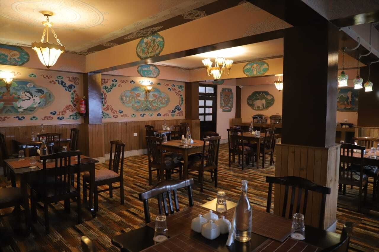 A restaurant with wooden floors, tables, and chairs, decorated with traditional wall art.