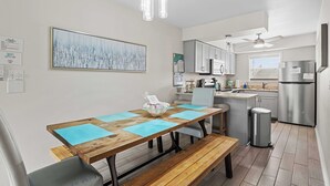 Moderni keittiö, jossa on puinen ruokapöytä, siniset aluslautasliinat ja ruostumattomasta teräksestä valmistetut kodinkoneet.