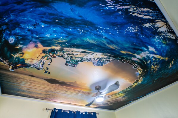 Un techo con un mural de olas y un ventilador de techo.