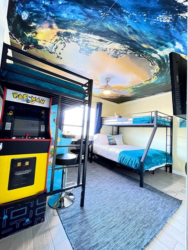 A room with bunk beds, a Pac-Man arcade machine, and a mural of a seascape on the ceiling. - Steps to Beach~ Gulf View~ Pool~ Arcades~ King Bed (Pensacola Beach)