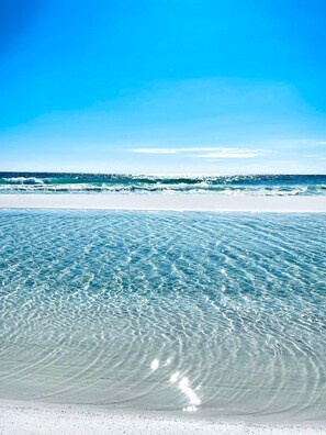 Una playa con aguas poco profundas y cristalinas, y una orilla arenosa bajo un cielo azul despejado.