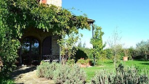 A stone building with a covered patio area, surrounded by lush greenery and a well-maintained garden.