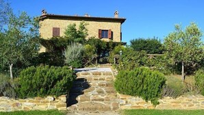 A stone pathway leading to a rustic stone building with a tiled roof and wooden shutters.