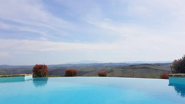 A clear blue infinity pool with a view of rolling hills and mountains in the distance.