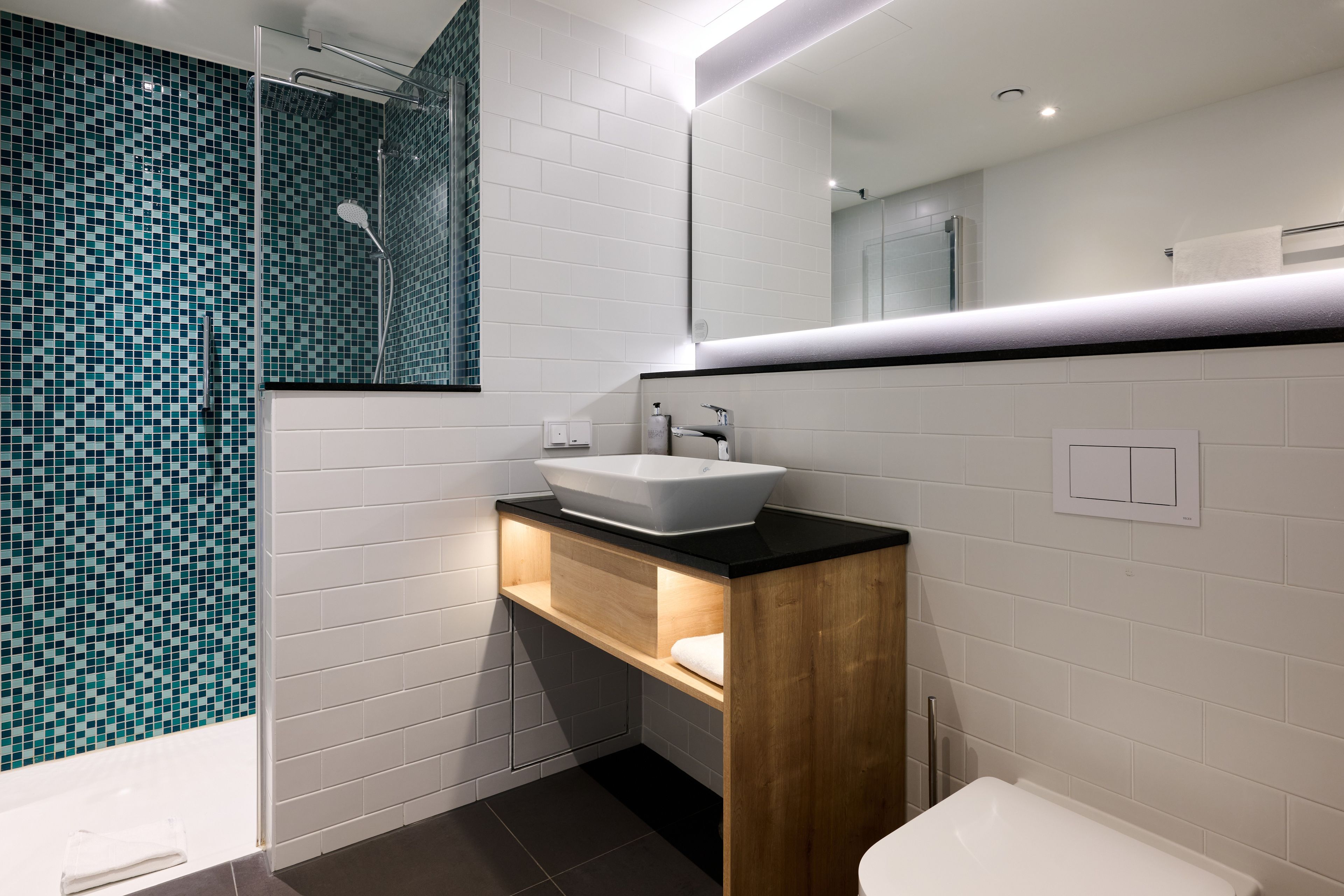 Une salle de bain moderne avec un lavabo blanc, un meuble-lavabo en bois et une douche aux carreaux de mosaïque bleus.