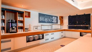 A breakfast area with a coffee machine, mugs, and a sign that reads 'BREAKFAST.'