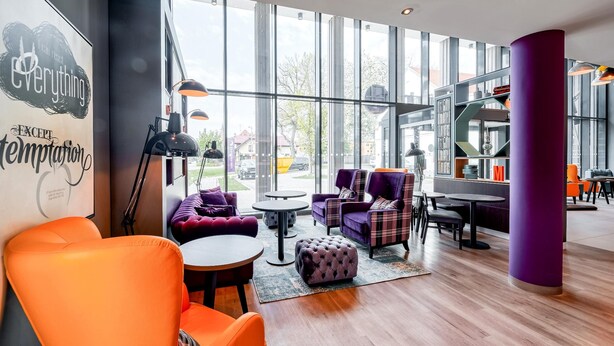 A modern interior with large windows, a purple sofa, a round table, and a purple pillar.
