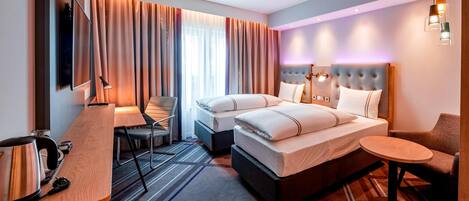 Ein Hotelzimmer mit einem Bett, zwei Nachttischen, einem Schreibtisch mit Stuhl, einem Fernseher und einem kleinen runden Tisch.
