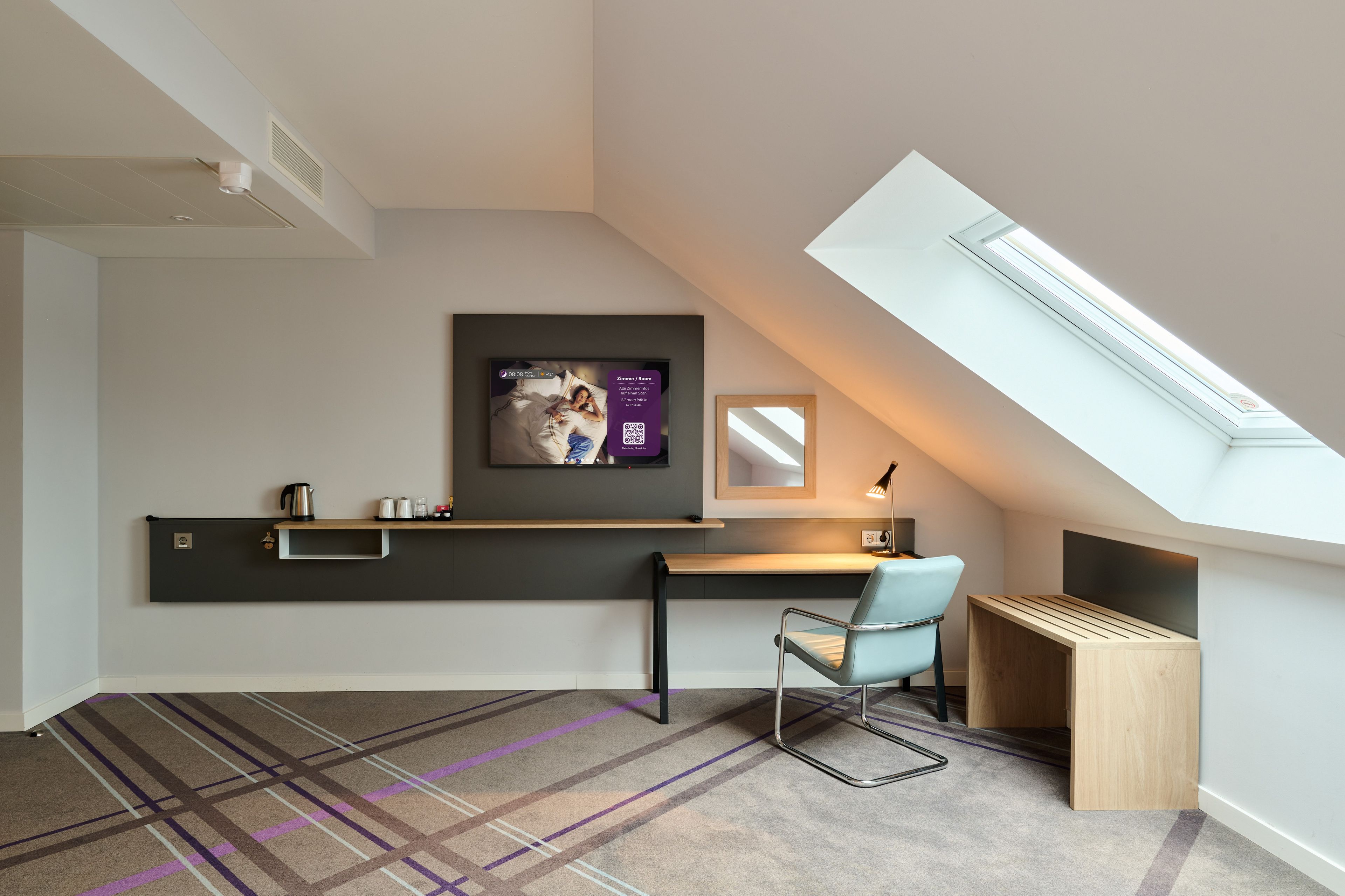 Una habitación moderna y compacta con techo inclinado, escritorio integrado, una silla, una mesita y un ventanal grande.