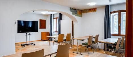 A conference room with tables and chairs, a flat-screen TV, and a window with curtains.