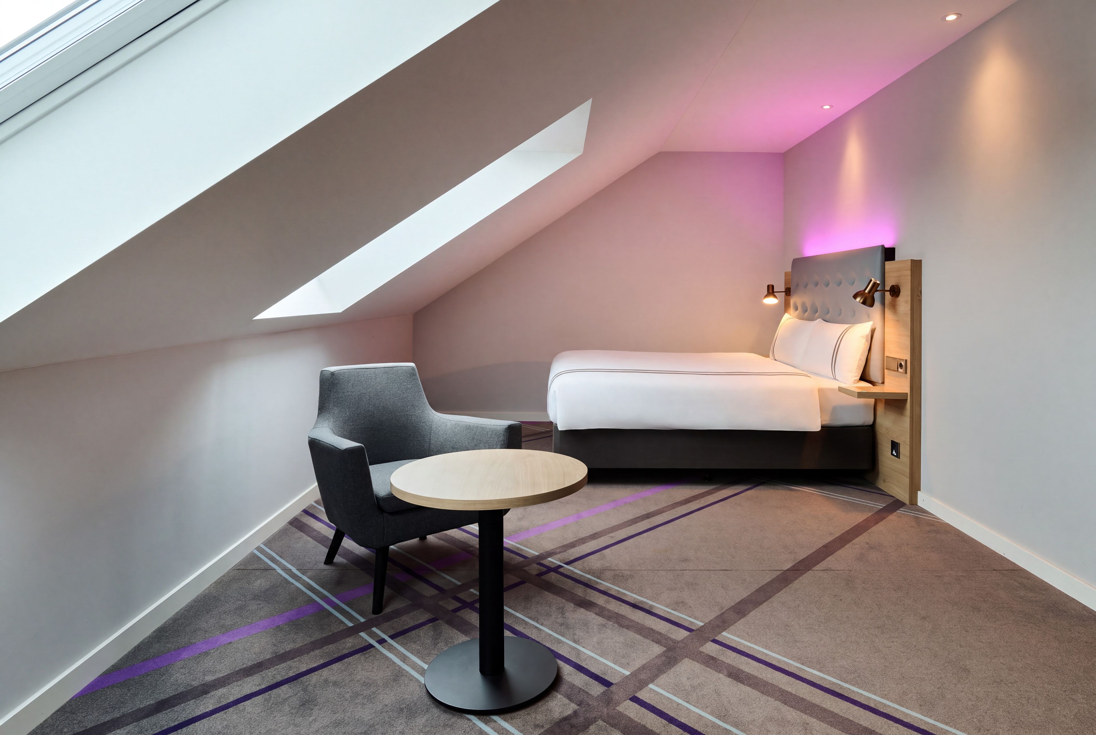 A compact room with a sloped ceiling, a bed, a chair, and a small table.