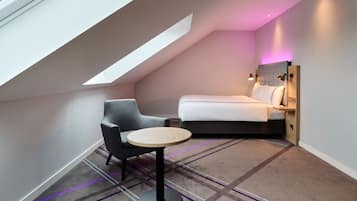 A compact room with a sloped ceiling, a bed, a chair, and a small table.