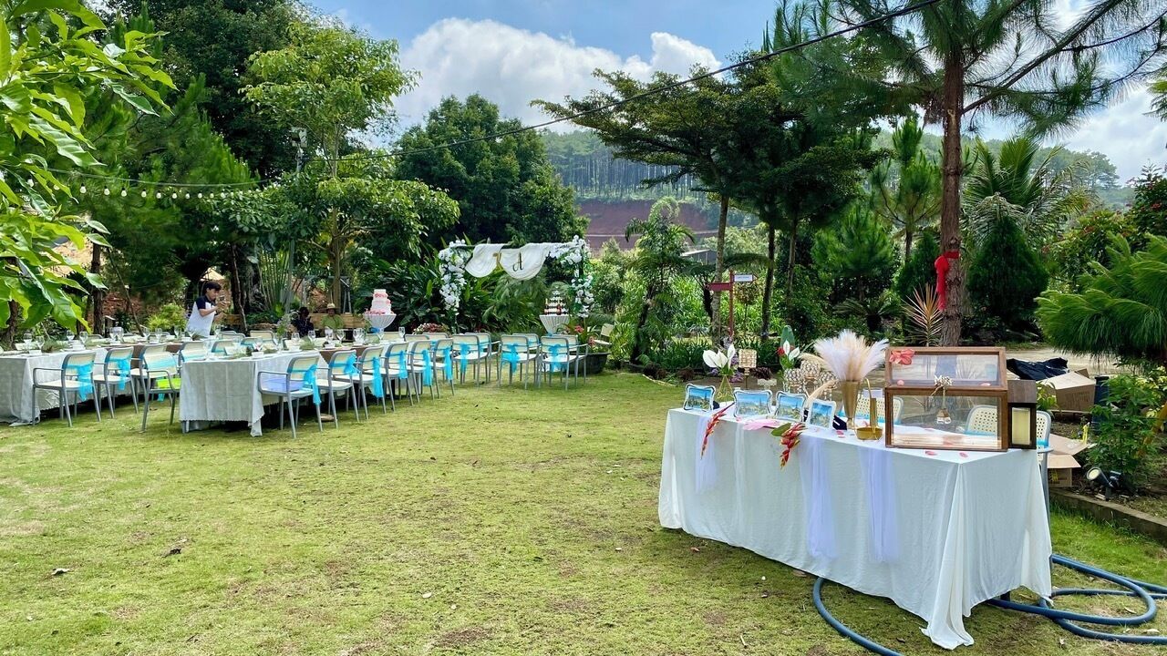 An outdoor event space with tables and chairs arranged for guests, surrounded by lush greenery and a view of a distant landscape.