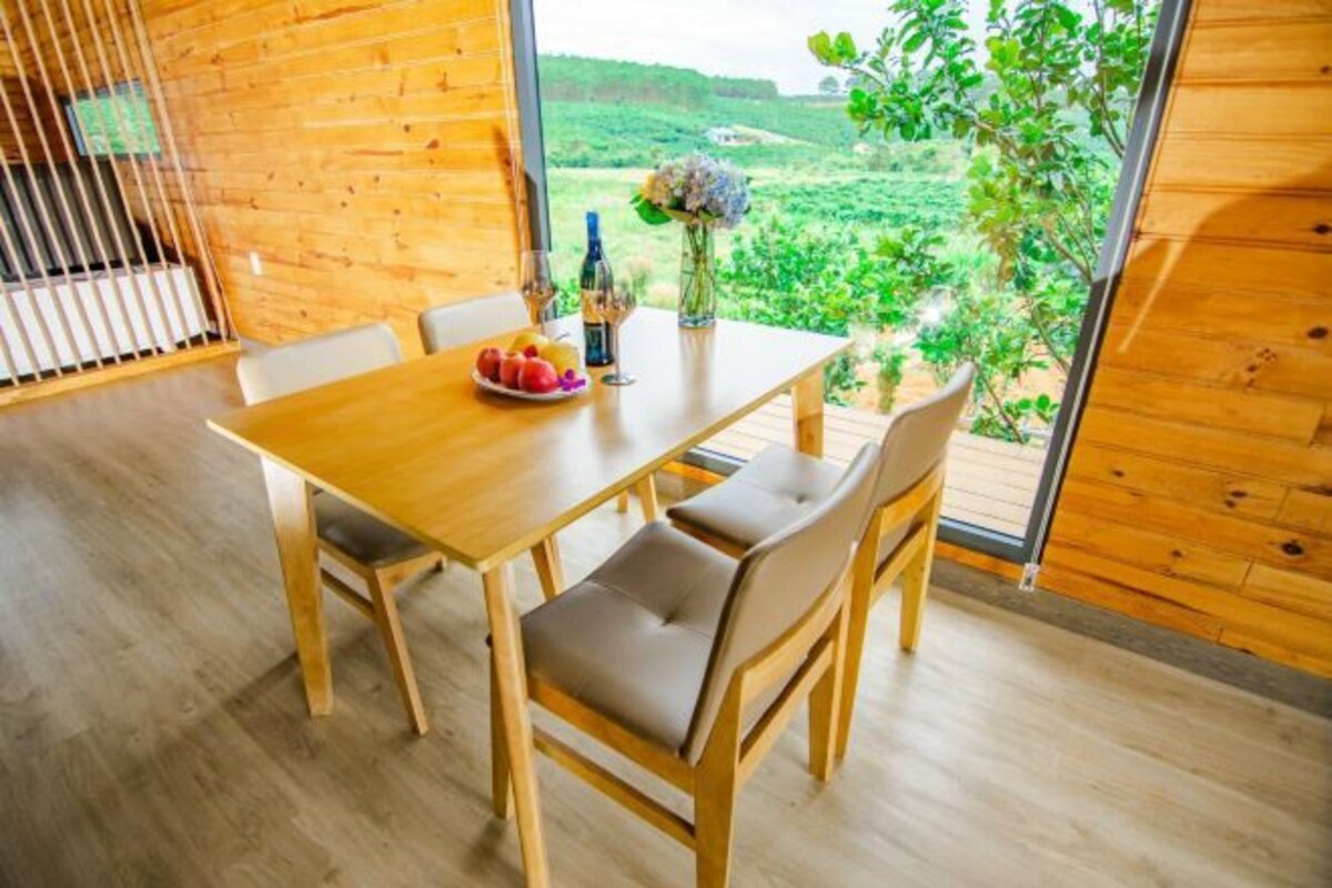 A wooden dining table with four chairs, a vase with flowers, and a plate of fruit.