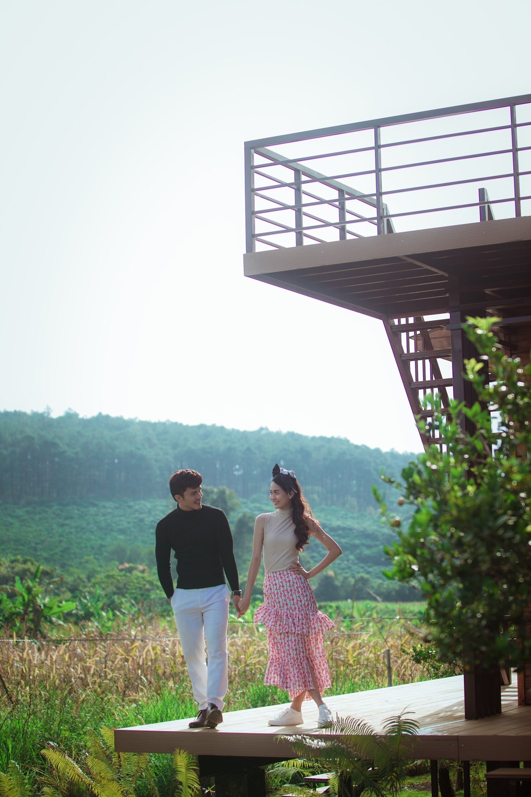 A couple holding hands on a wooden deck with a view of a forested landscape.
