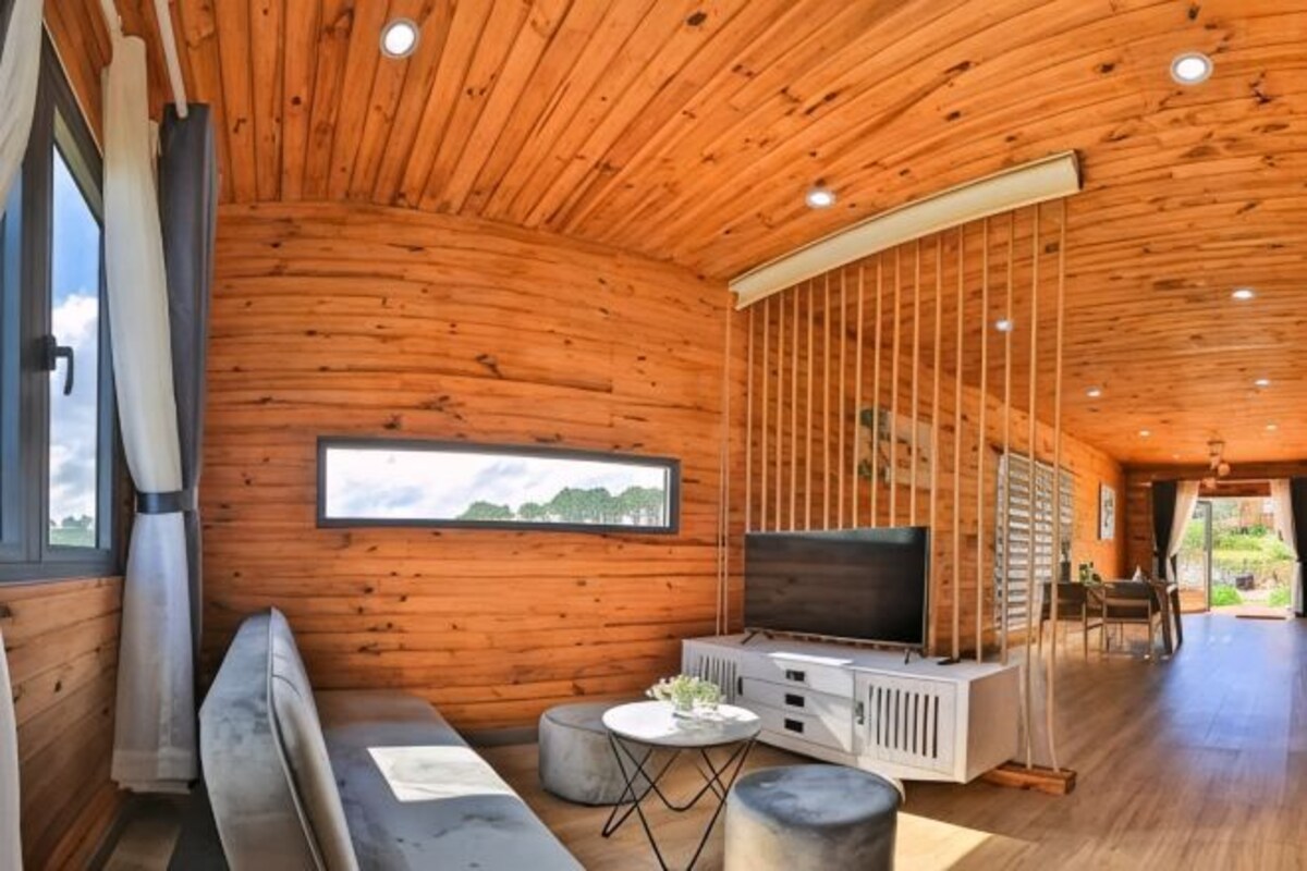 A log cabin interior with a wooden ceiling, a sofa, a TV, and a dining area.