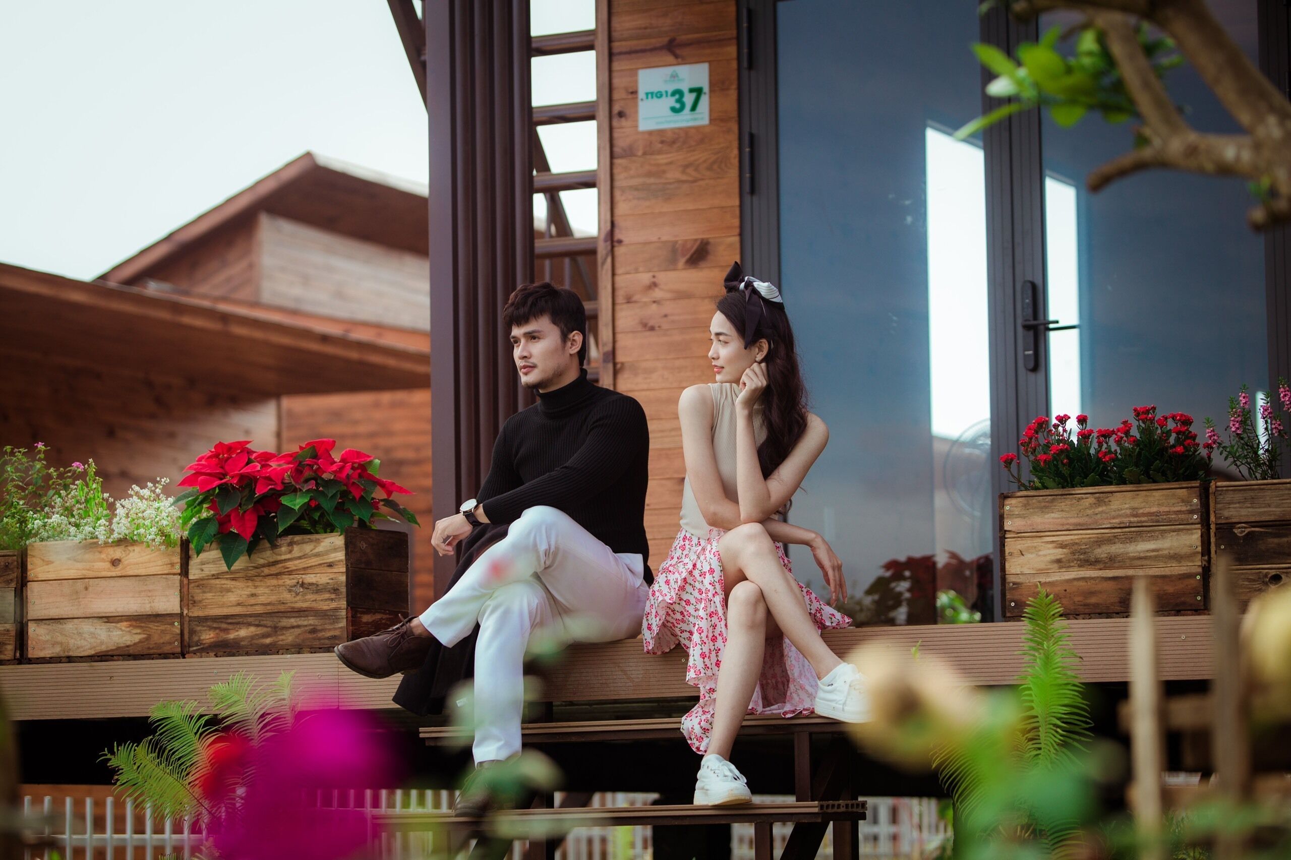 Two people sitting on a wooden bench outside a building with wooden walls and a sign indicating room number 37.