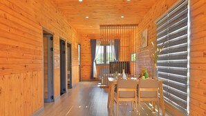 A wooden interior with a dining area featuring a table and chairs, a window with blinds, and a ceiling with recessed lighting.