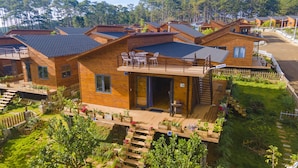 A modern wooden cabin with a balcony, surrounded by lush greenery and a wooden deck.