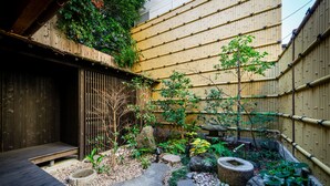 Un giardino tradizionale giapponese con un pontile in legno, una recinzione di bambù e diverse piante.