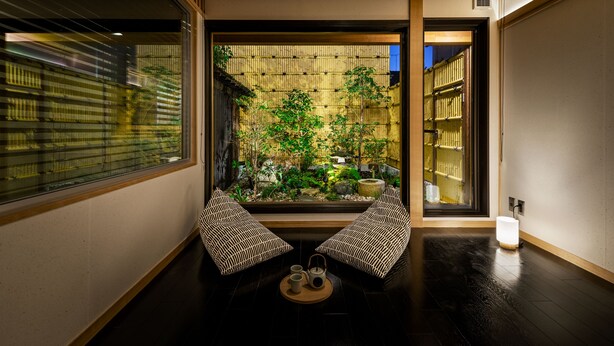 Una tradizionale stanza giapponese con pavimento in tatami, un tavolino con un servizio da tè e vista su un giardino di bambù attraverso un'anta scorrevole.