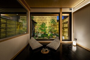 A traditional Japanese room with tatami flooring, a low table with a tea set, and a view of a bamboo garden through a sliding door.