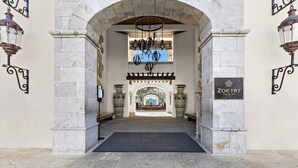 An entrance with a stone archway, a chandelier, and a sign for 'ZOETRY CASA DEL MAR BY AMAR COLLECTION'.