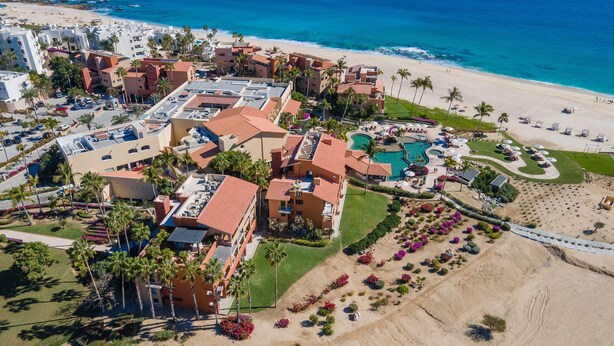 An aerial view of a resort with multiple buildings, a large swimming pool, and a beach area.