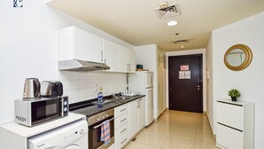A compact kitchen with white cabinets, a microwave, a kettle, and a washing machine. - BRZ - Budget studio with balcony (Dubai)